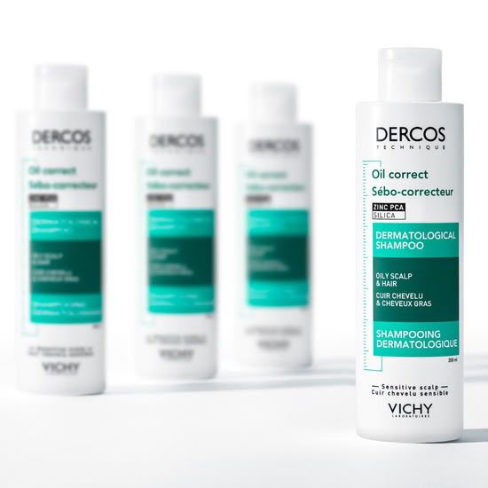 Steklenička dermatološkega šampona Vichy Dercos Oil Correct za mastno lasišče in lase, postavljena v ospredju s tremi zamegljenimi stekleničkami v ozadju.